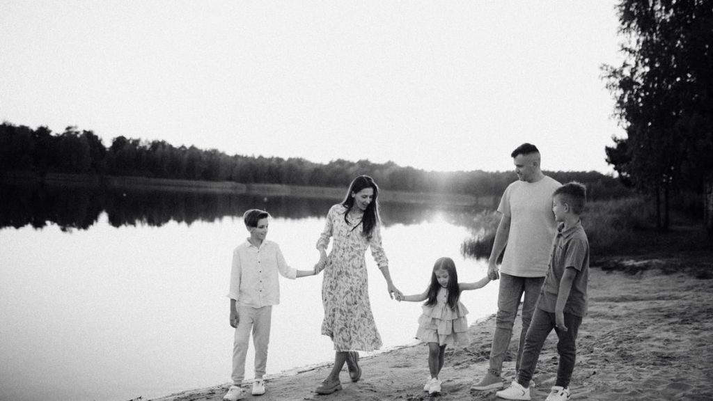 Monochrome photo of a family walking hand in hand along a serene lakeshore.