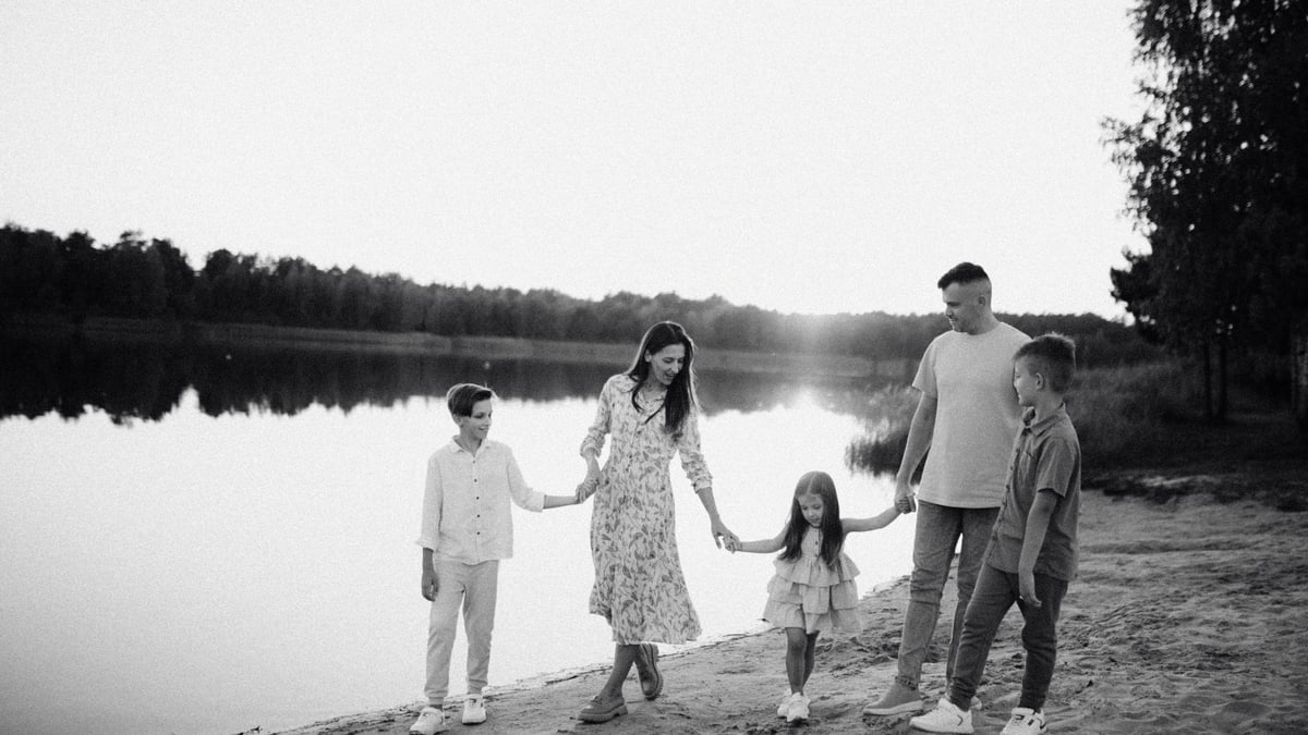 Monochrome photo of a family walking hand in hand along a serene lakeshore.